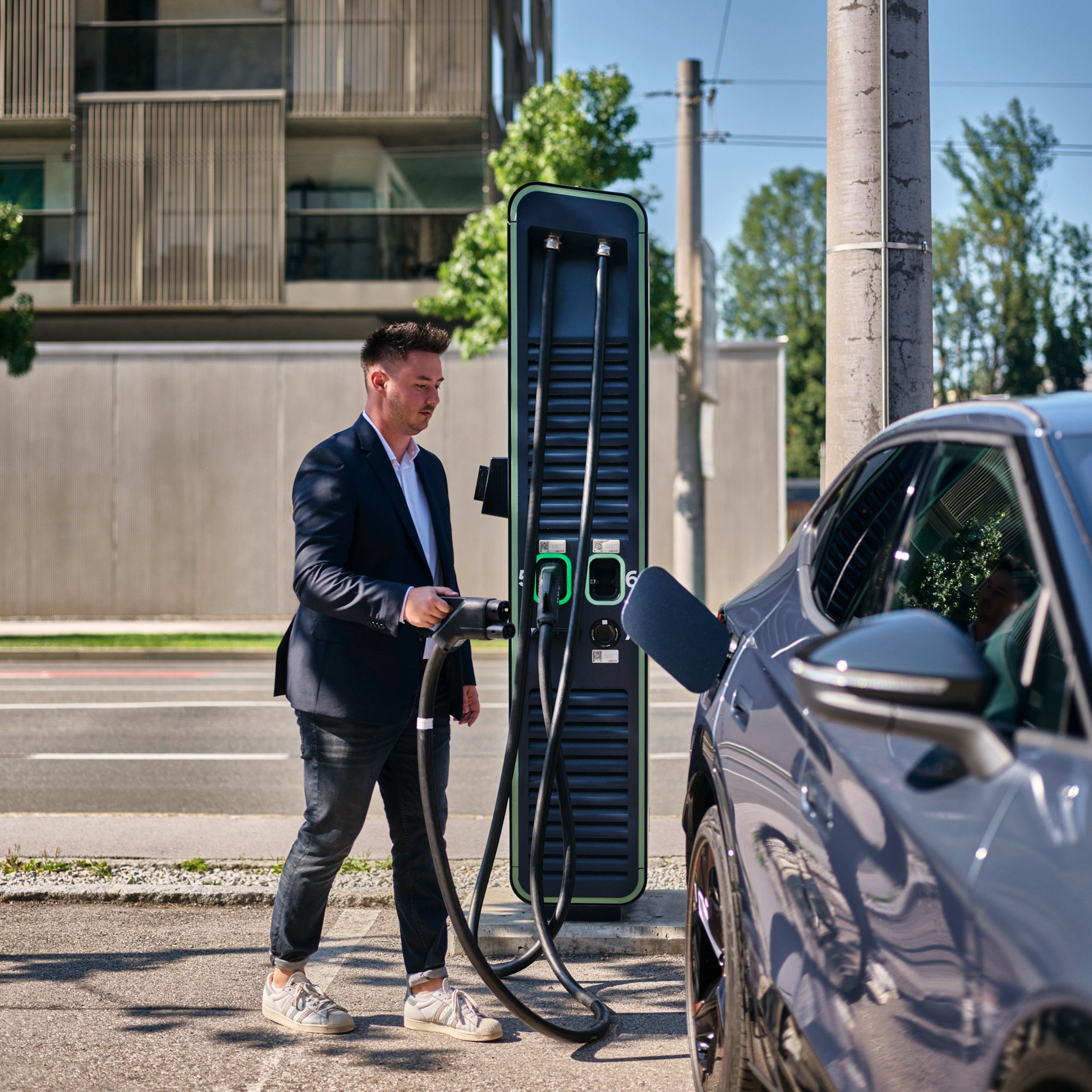 Mann hält Zapfventil einer Schnellladestation in der Hand und geht auf ein E-Auto zu