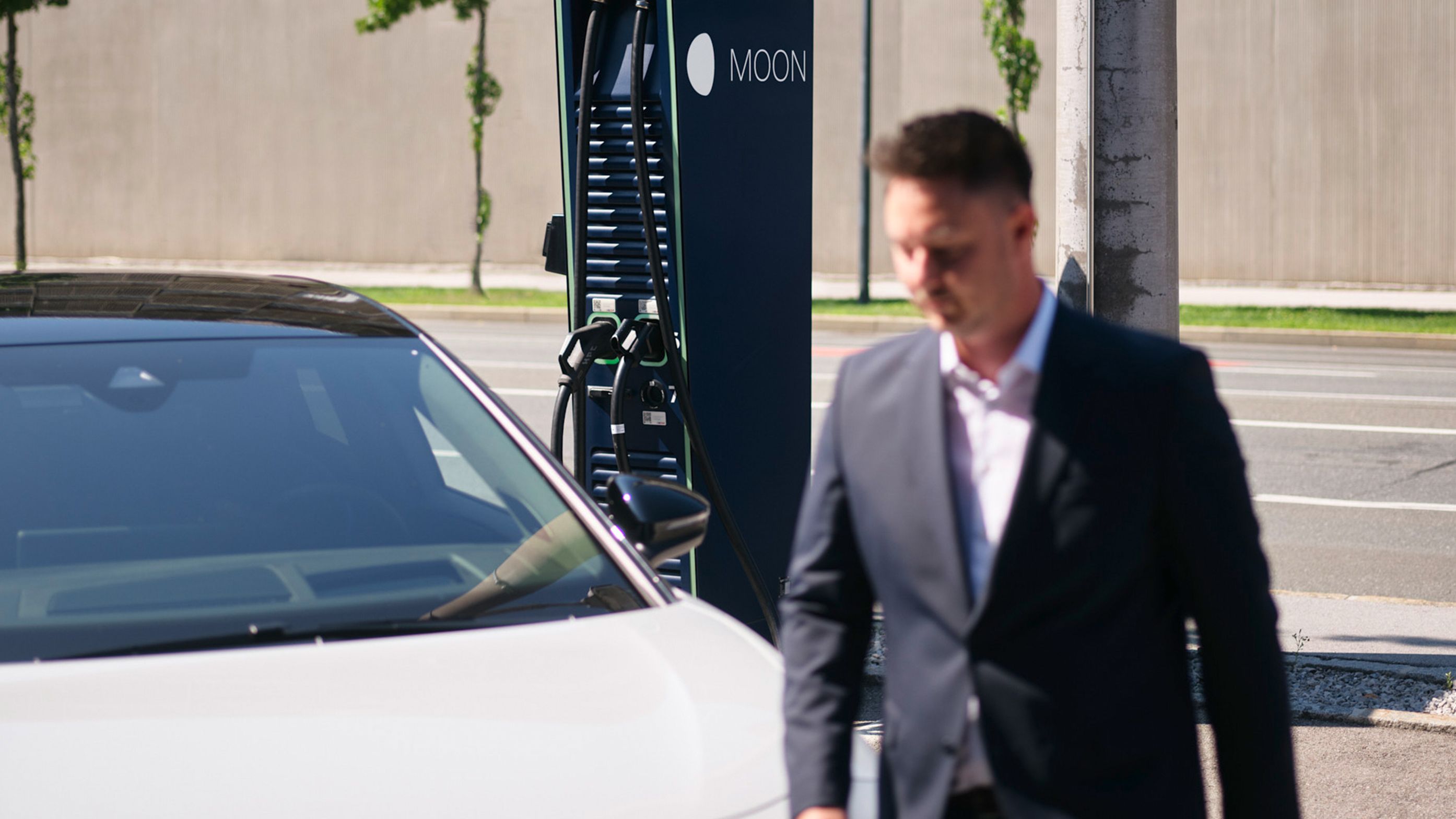 Mann geht vor einem E-Auto vor einer Schnellladestation vorbei