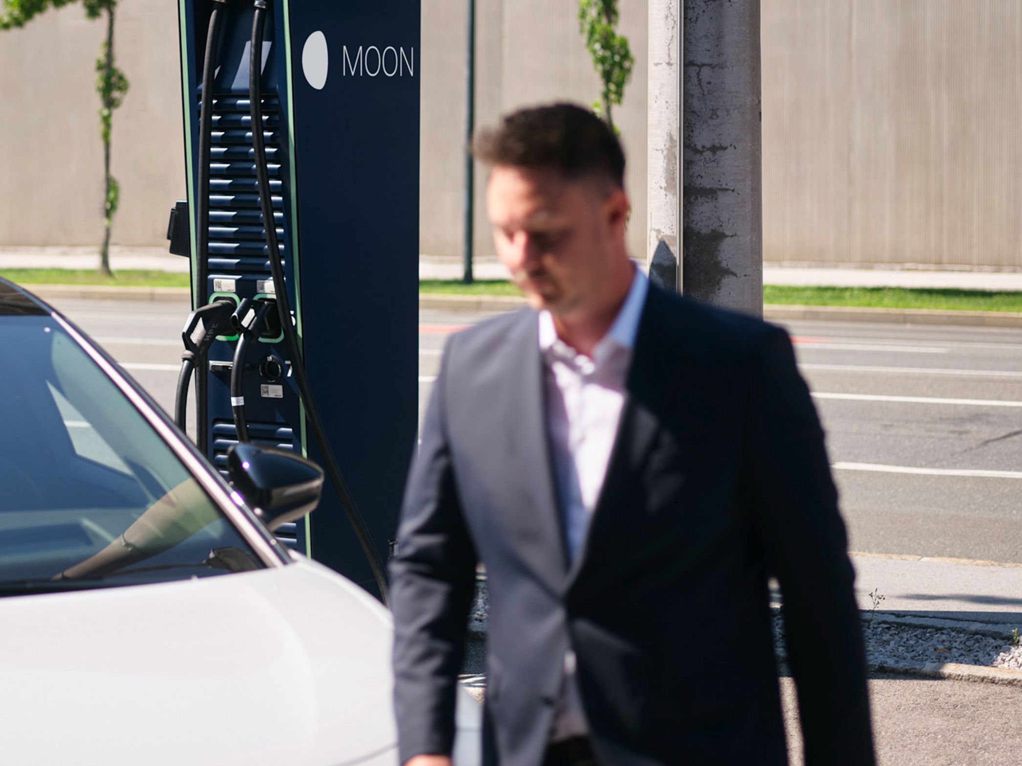 Mann geht vor einem E-Auto vor einer Schnellladestation vorbei