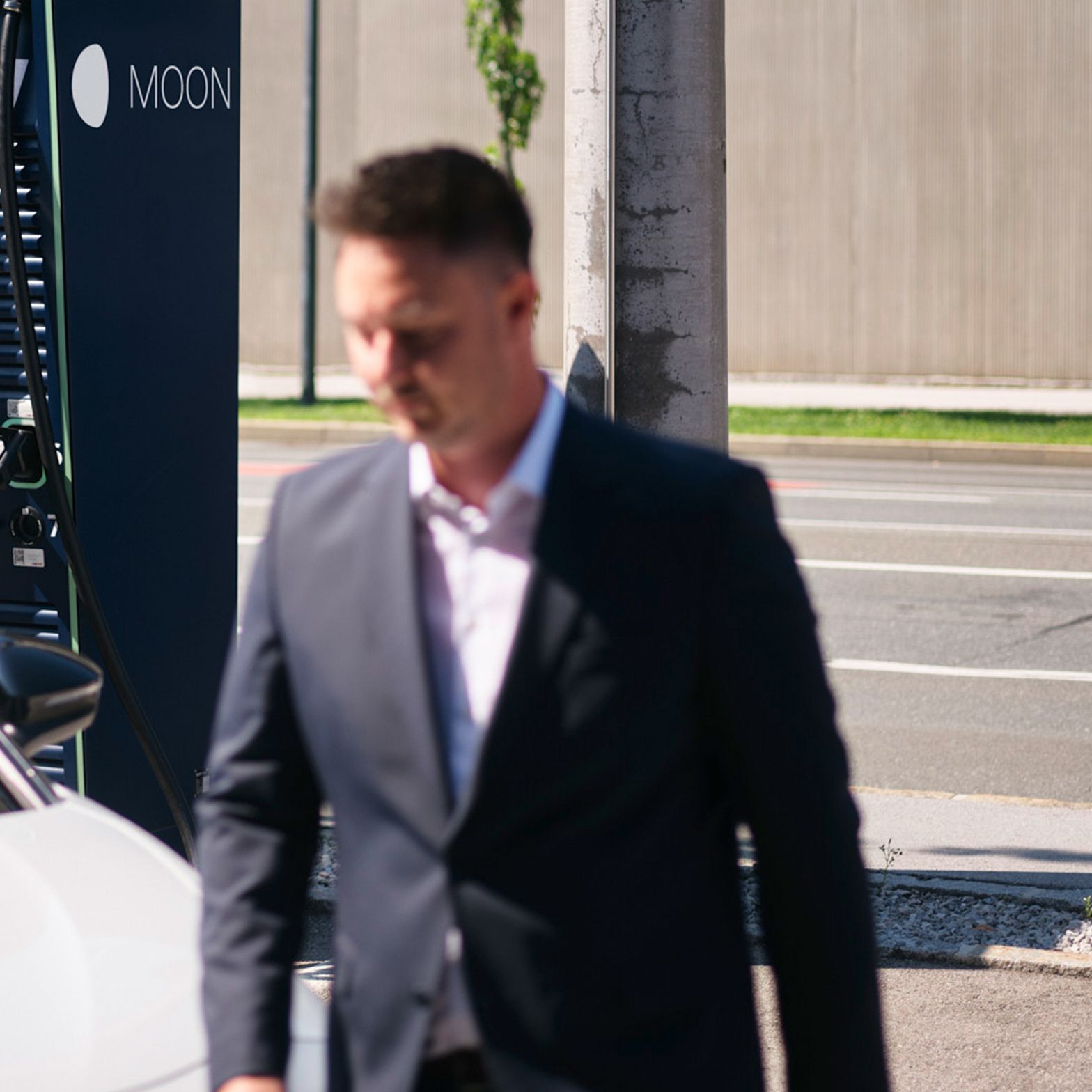 Mann geht vor einem E-Auto vor einer Schnellladestation vorbei