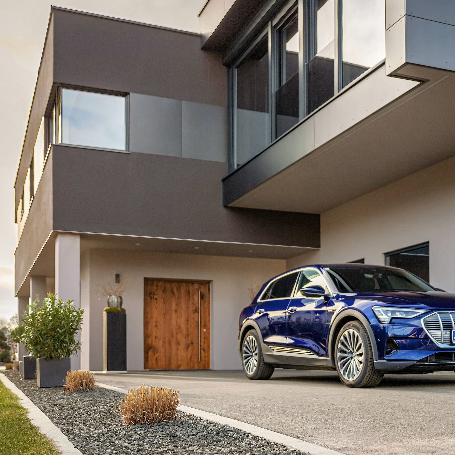 Mann geht mit einem Kabel in der Hand auf ein E-Auto bei einem Haus zu