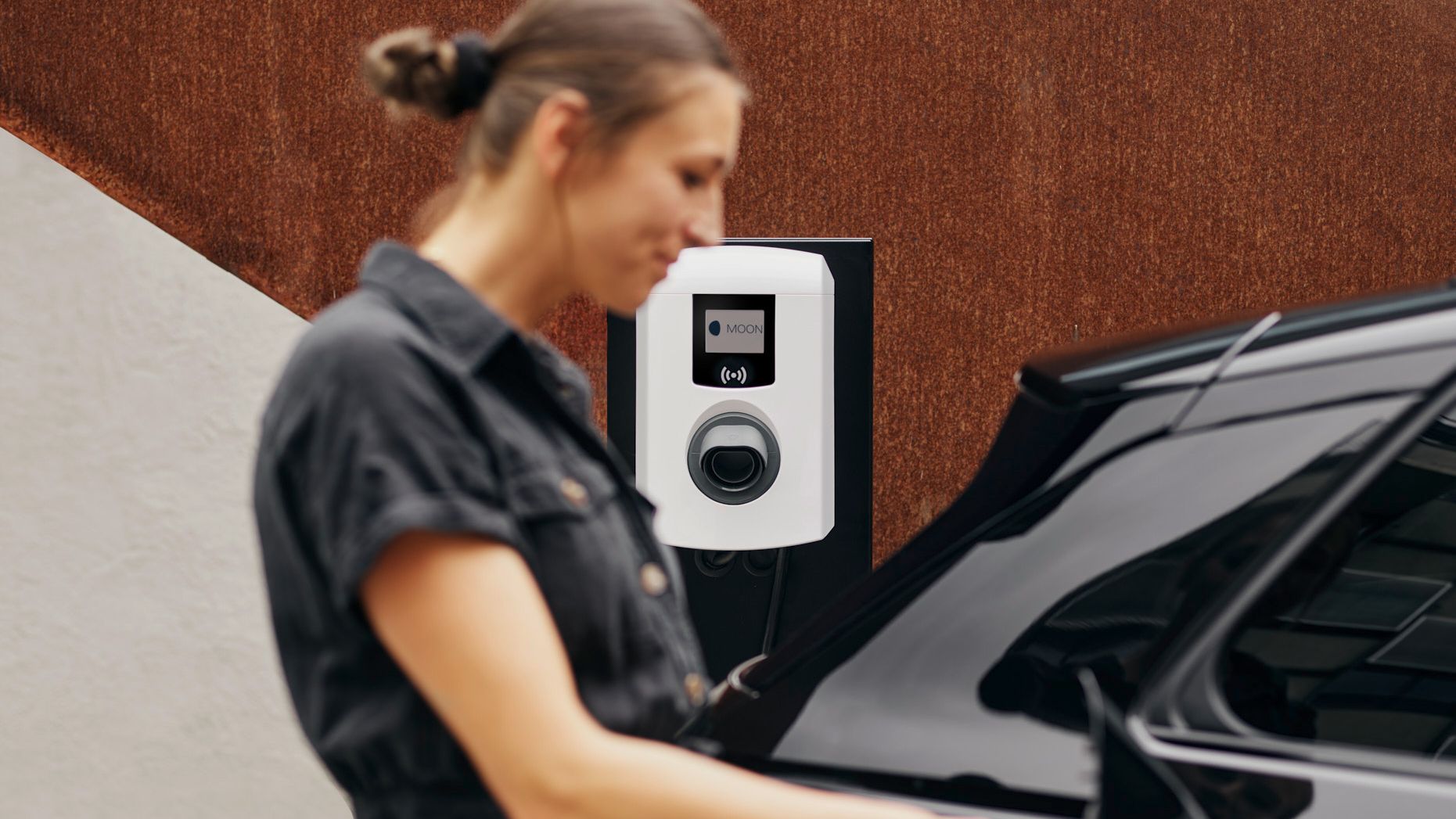 Frau steckt Zapfventil einer Wallbox in ein E-Auto