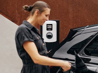 Person steckt Zapfventil einer Wallbox in ein E-Auto