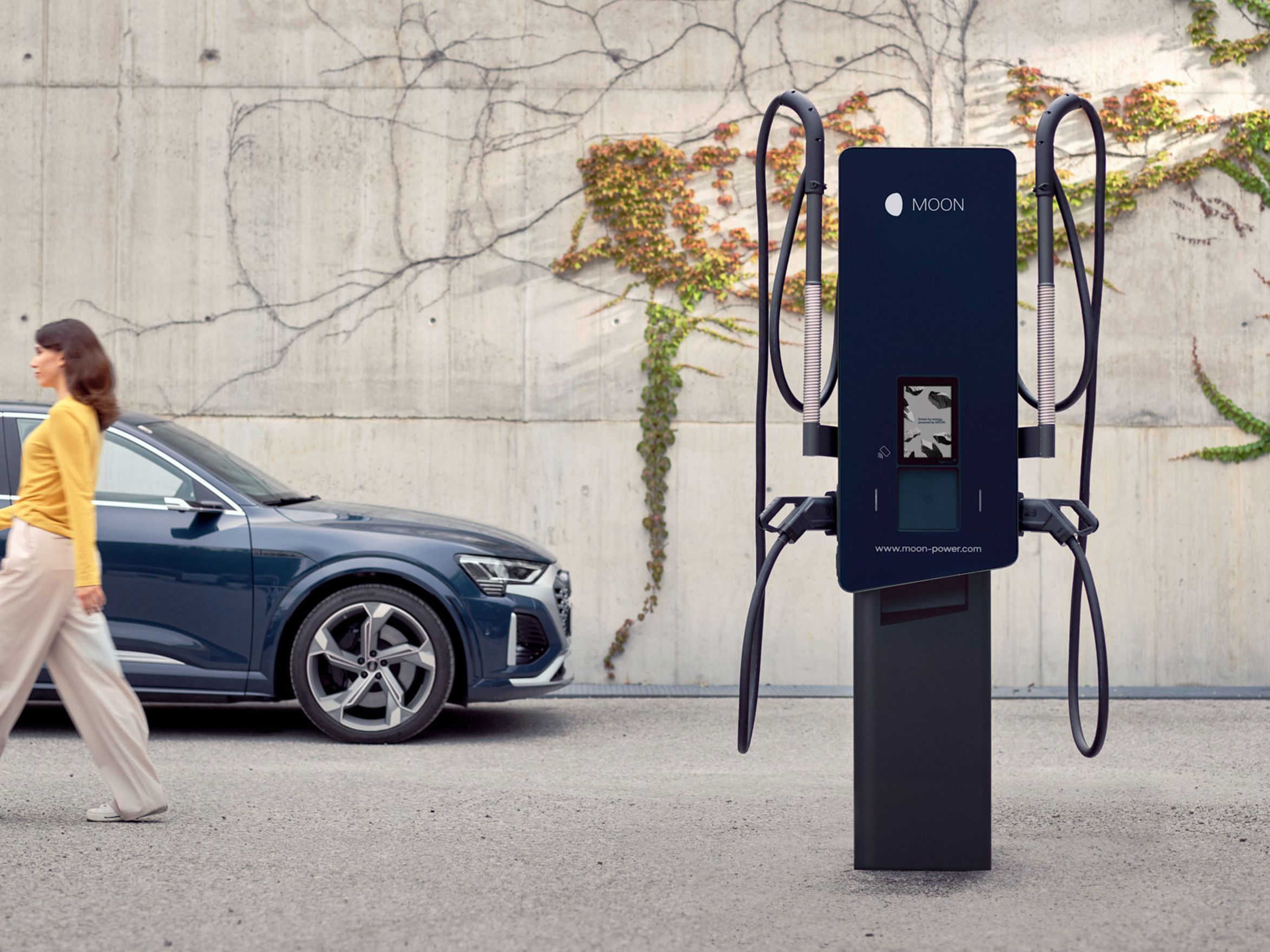 Frau geht von einer Wallbox weg an einem E-Auto vorbei