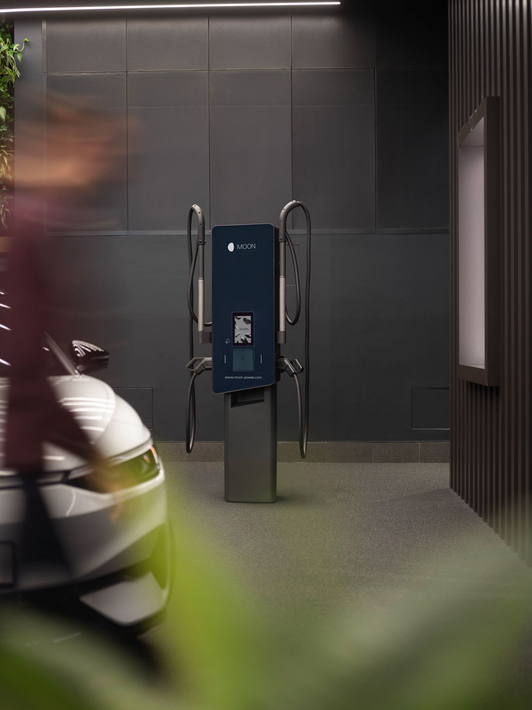 Wallbox vor einer grauen Wand mit E-Auto im Vordergrund