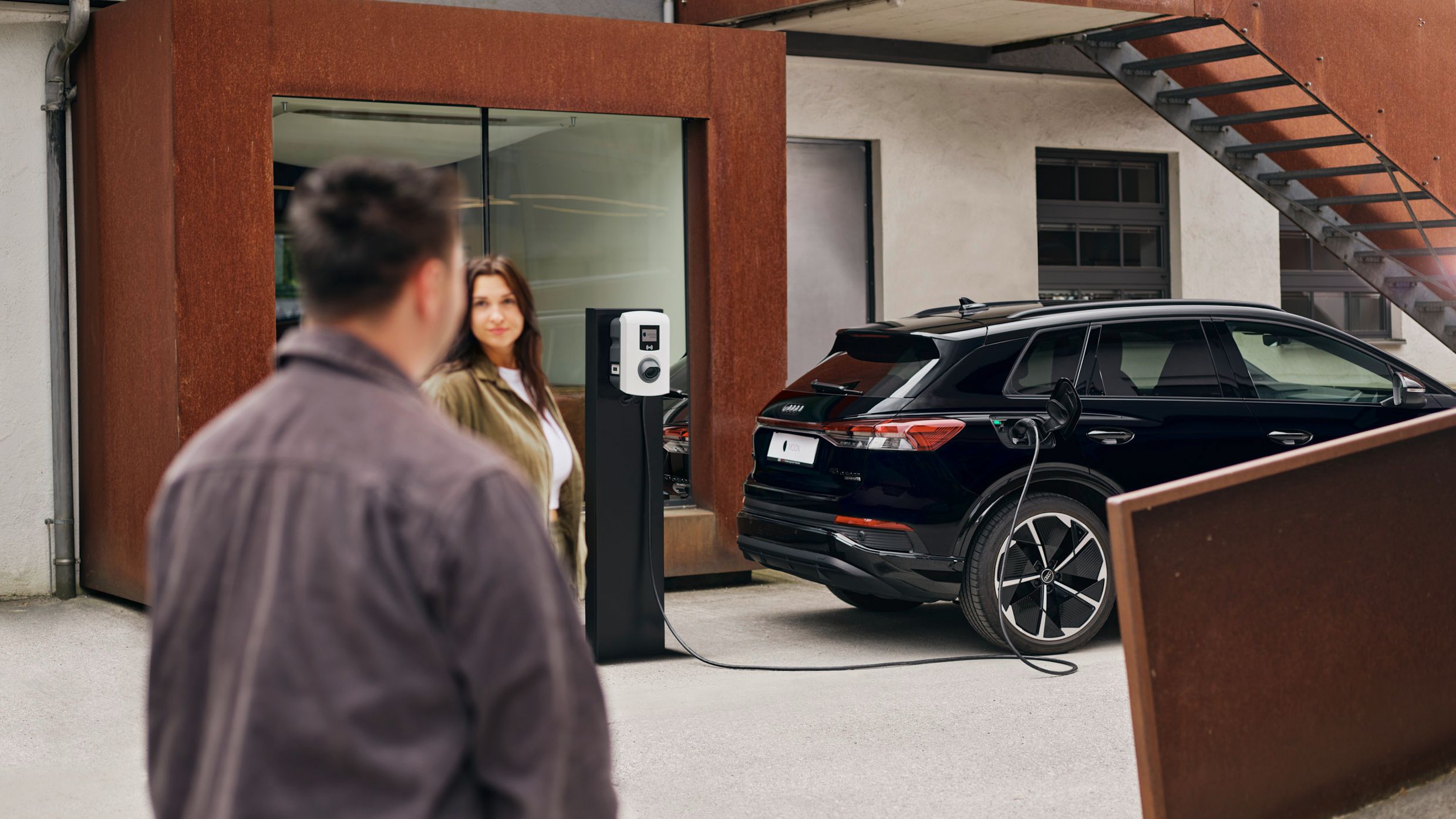 zwei Menschen stehen vor einer Wallbox die an E-Auto angesteckt ist