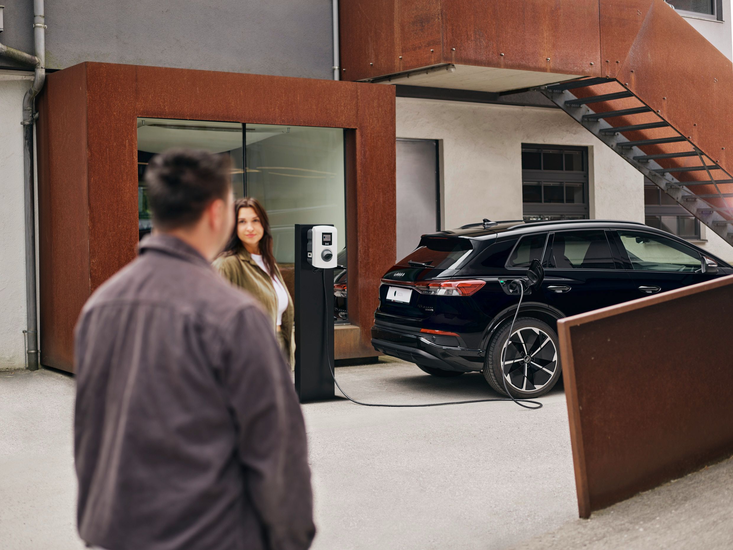 zwei Menschen stehen vor einer Wallbox die an E-Auto angesteckt ist