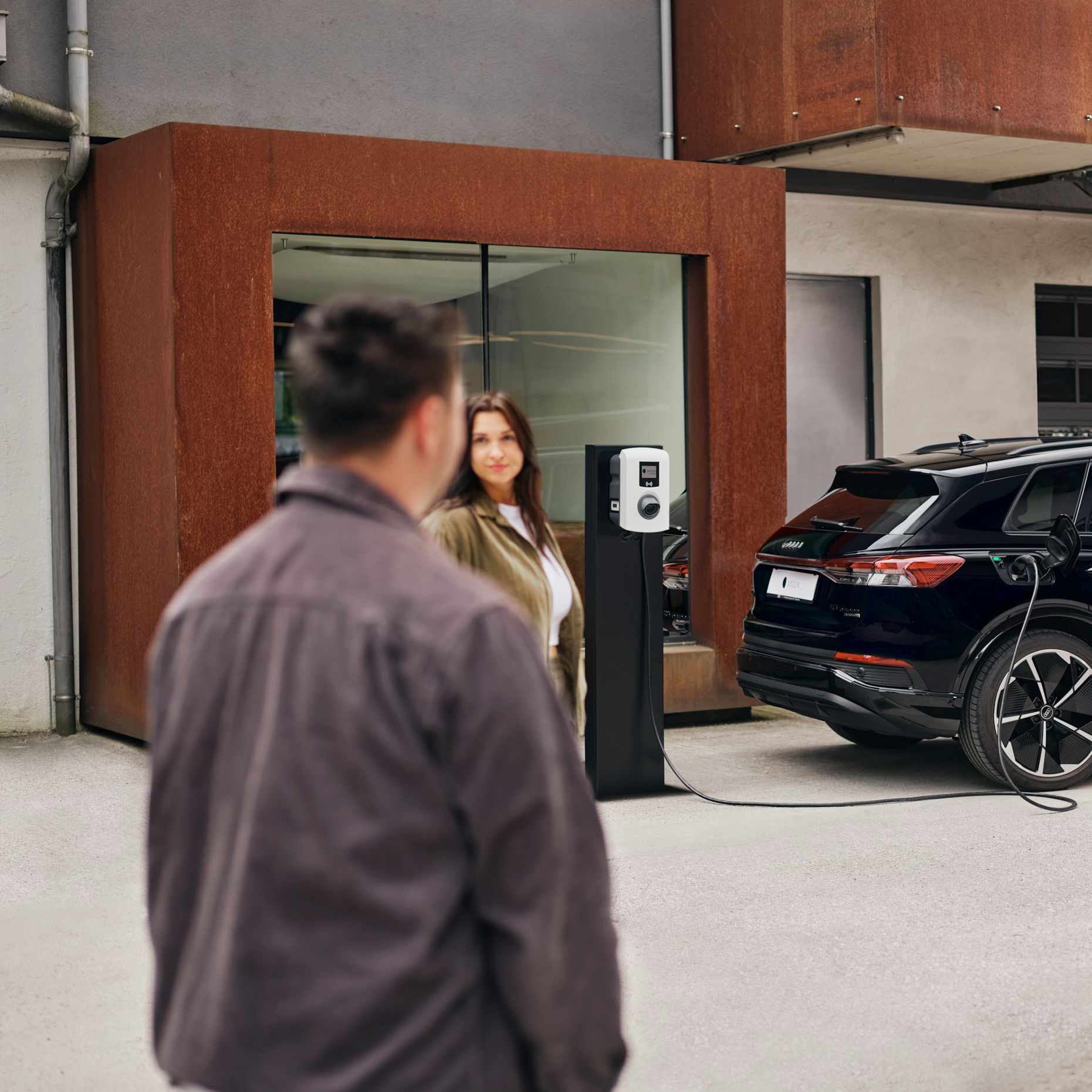 zwei Menschen stehen vor einer Wallbox die an E-Auto angesteckt ist