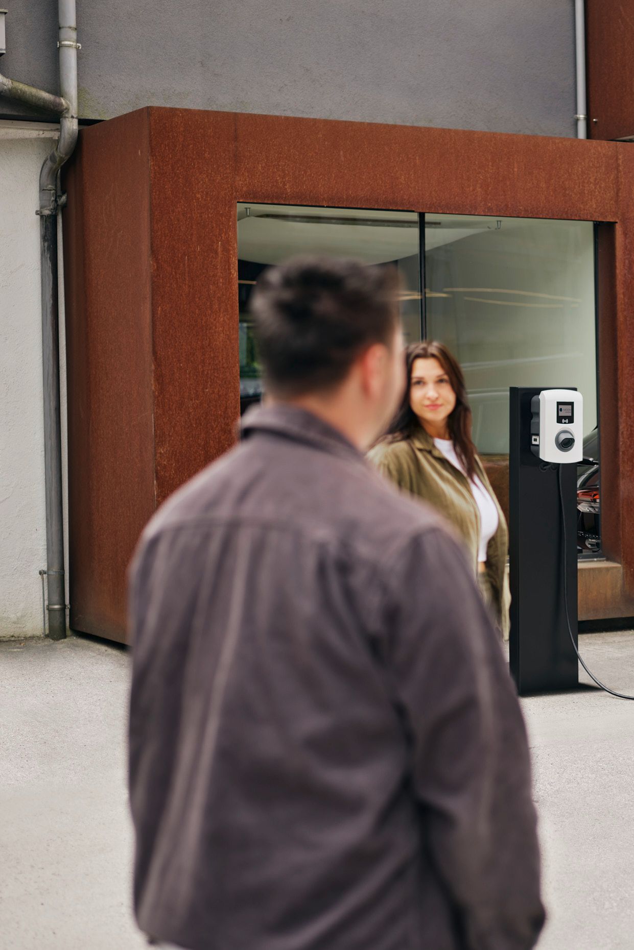 zwei Menschen stehen vor einer Wallbox die an E-Auto angesteckt ist