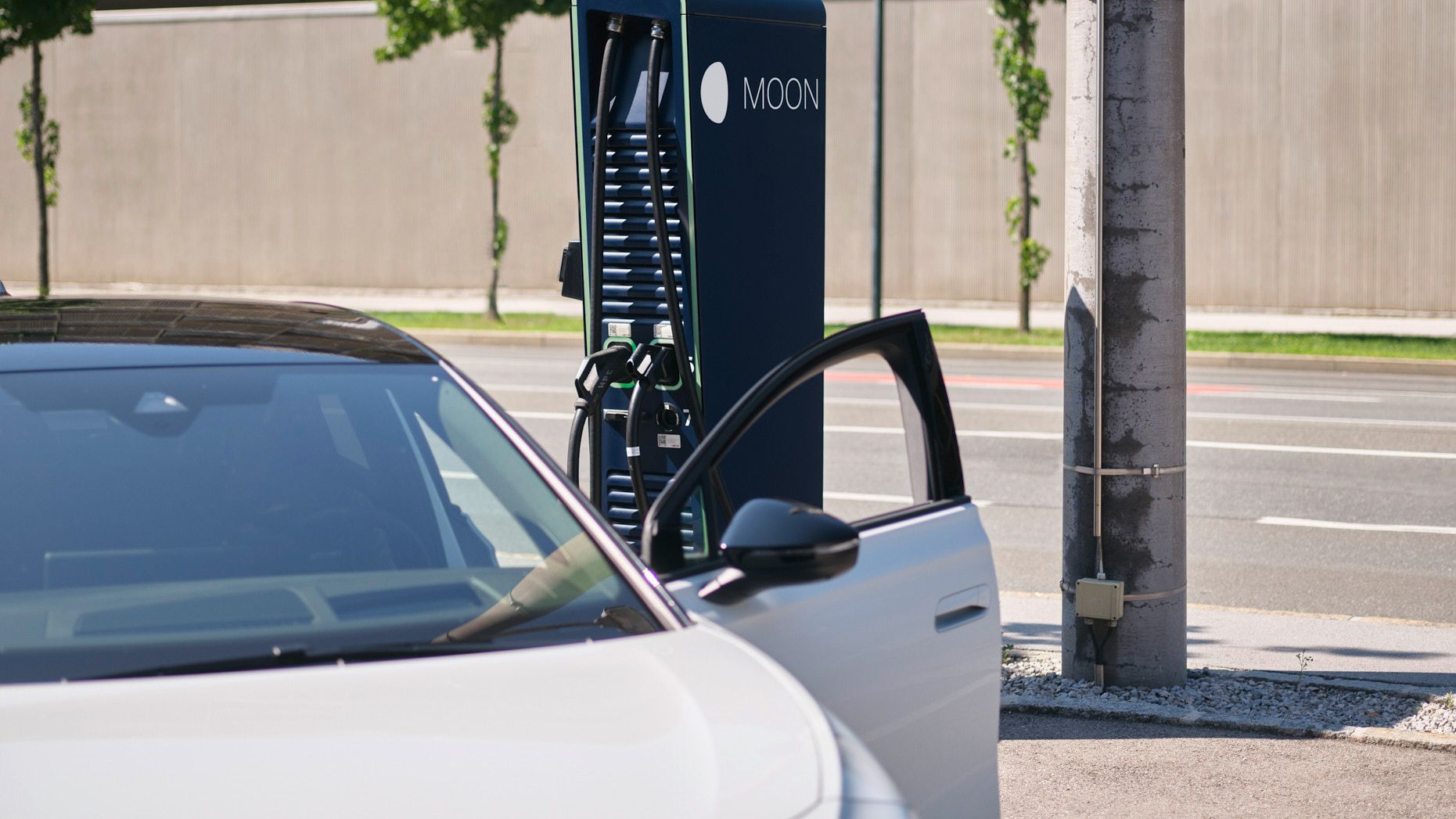 E-Auto steht vor einer Schnellladestation mit Straße im Hintergrund